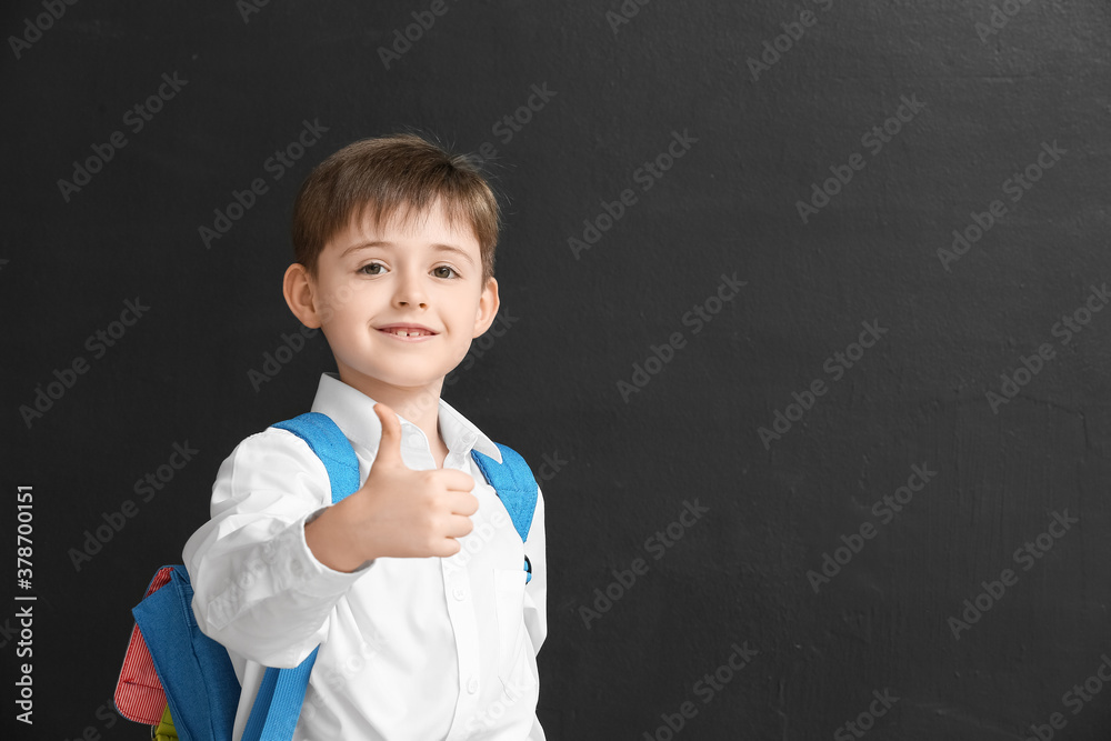 Little schoolboy showing thumb-up on dark background