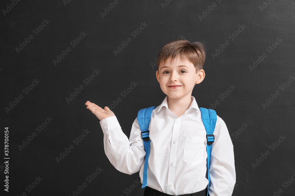 Little schoolboy showing something on dark background