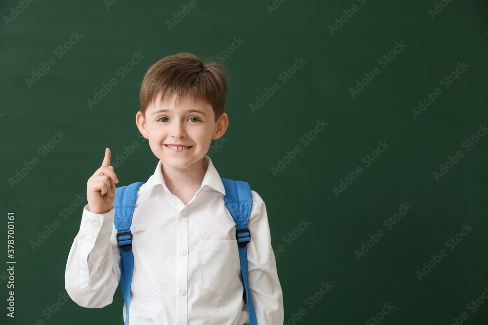 Little schoolboy with raised index finger on color background