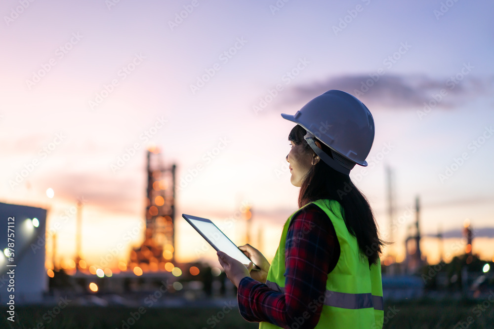 Asian woman petrochemical engineer working at night with digital tablet Inside oil and gas refinery 