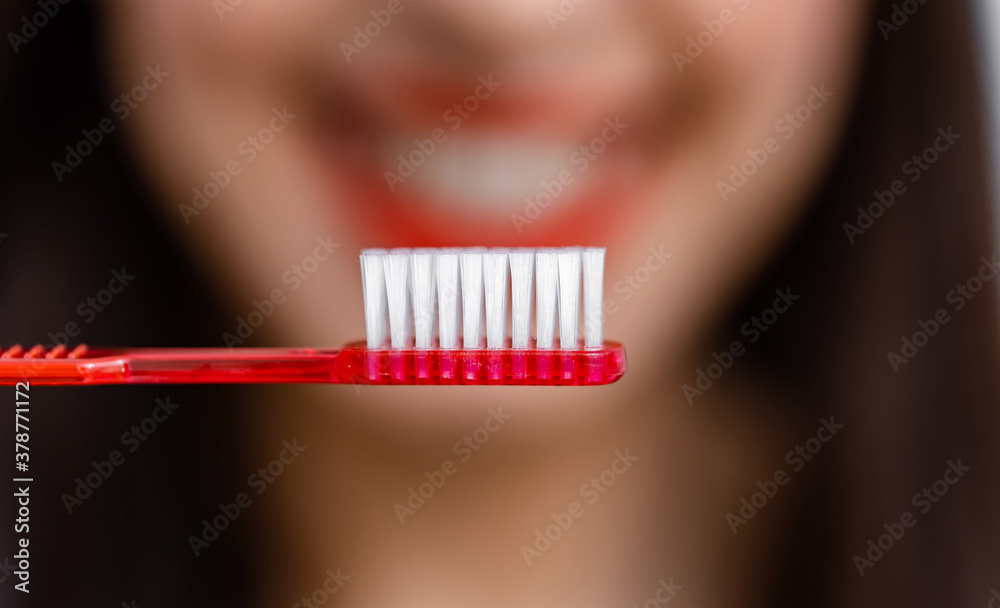 Smiling young woman with healthy teeth holds a toothbrush. Selective focus. Cropped photo. Blurred b