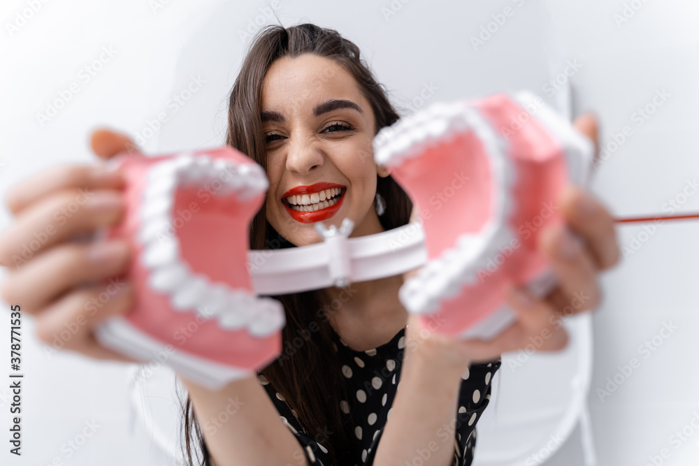 Funny girl with an opened dental jaw near face. Woman toing with plastic educational teeth model.