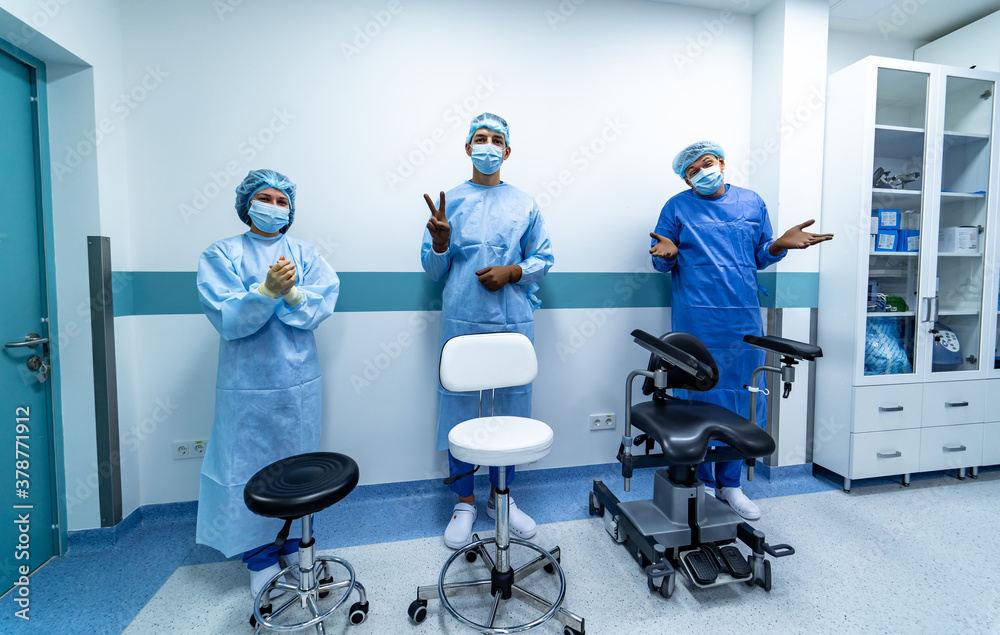 Three office chairs in hospital hall. Three doctors standing behind. Medics in scrubs.