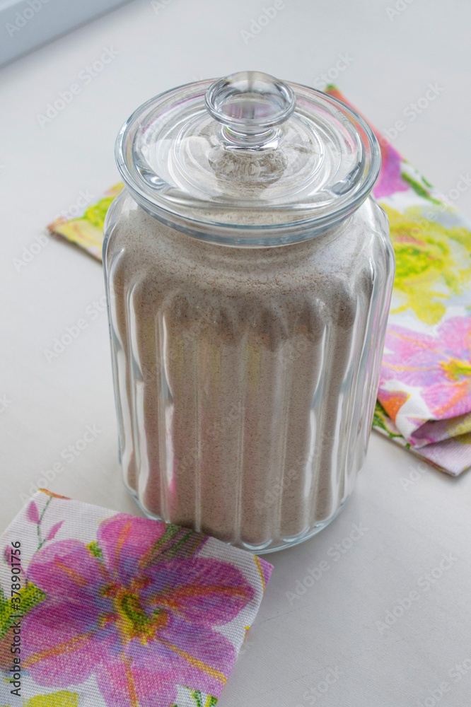 Composition in natural sunlight. Large glass jar of coarse bread flour and fragments of colored kitc