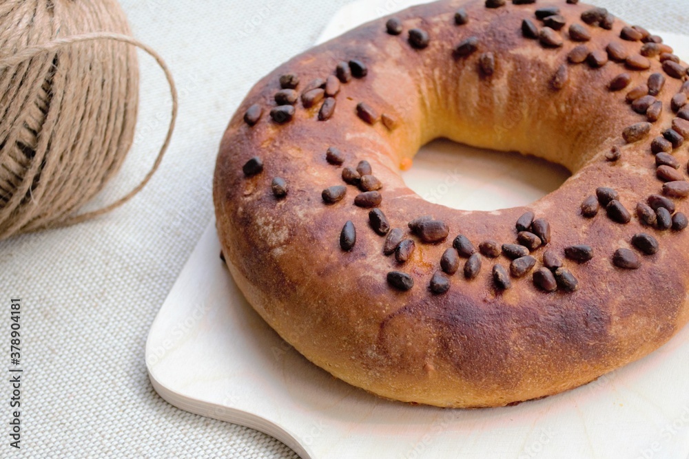 Composition in natural sunlight. Large homemade ruddy bagel with pine nuts on a wooden board, agains