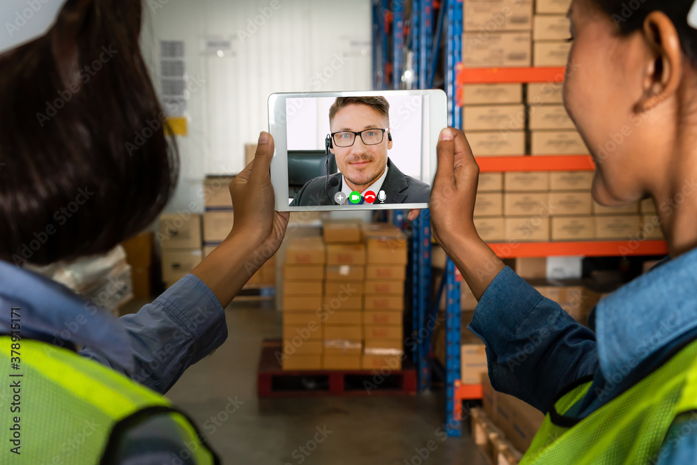 Warehouse staff talking on video call at computer screen in storage warehouse . Online software tech