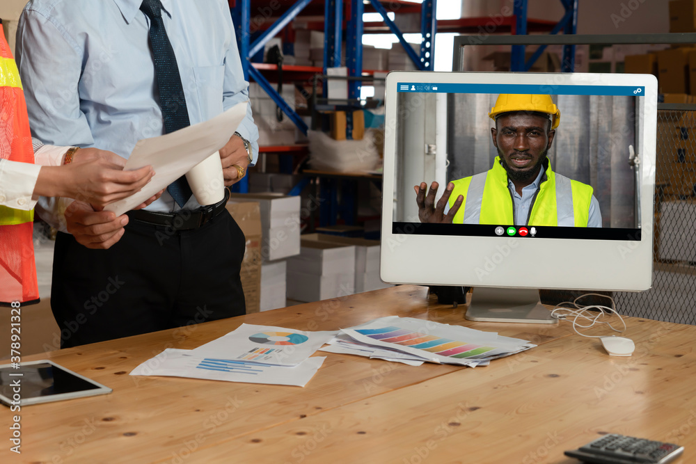 Warehouse staff talking on video call at computer screen in storage warehouse . Online software tech