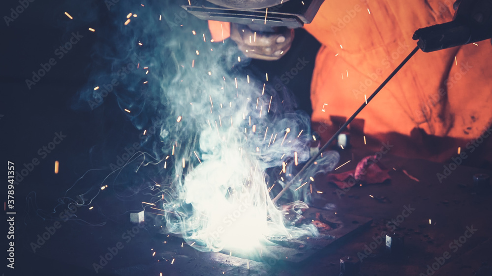 Metal welder working with arc welding machine to weld steel at factory while wearing safety equipmen