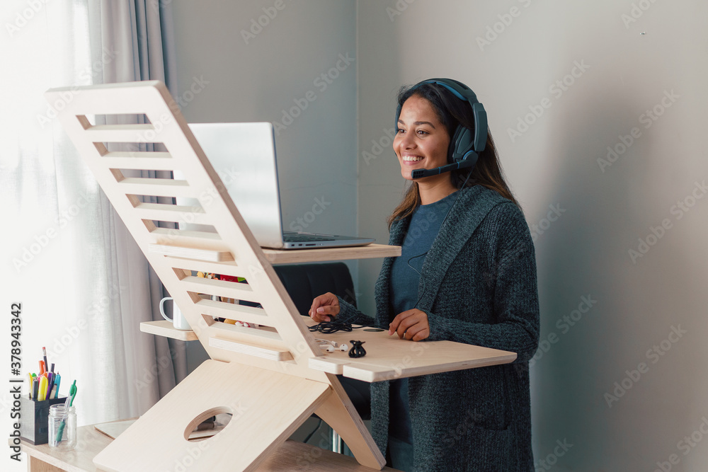 Young woman working on laptop at standing desk with earphones