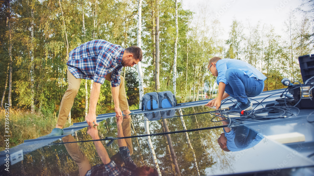 Father and Son Installing Solar Panels to a Metal Basis. They Work on a House Roof on a Sunny Day. C