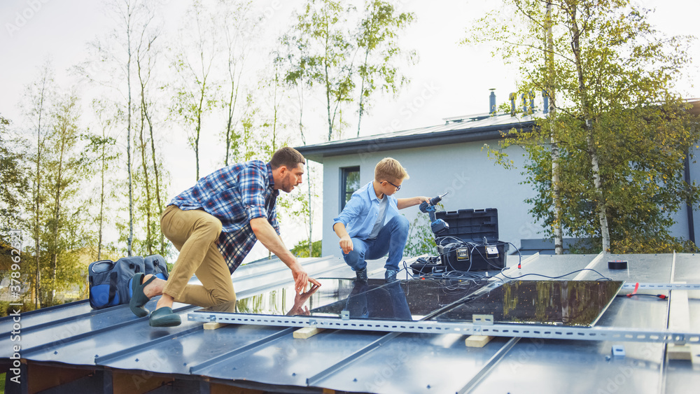 Father and Son Installing Solar Panels to a Metal Basis with a Drill. They Work on a House Roof on a