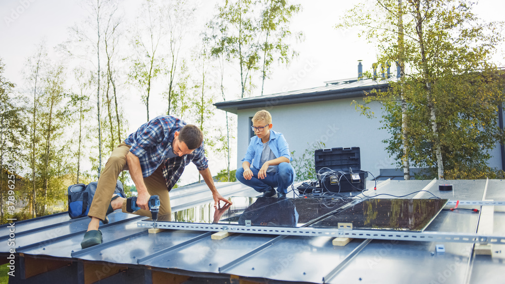 Father and Son Installing Solar Panels to a Metal Basis. They Work on a House Roof on a Sunny Day. C