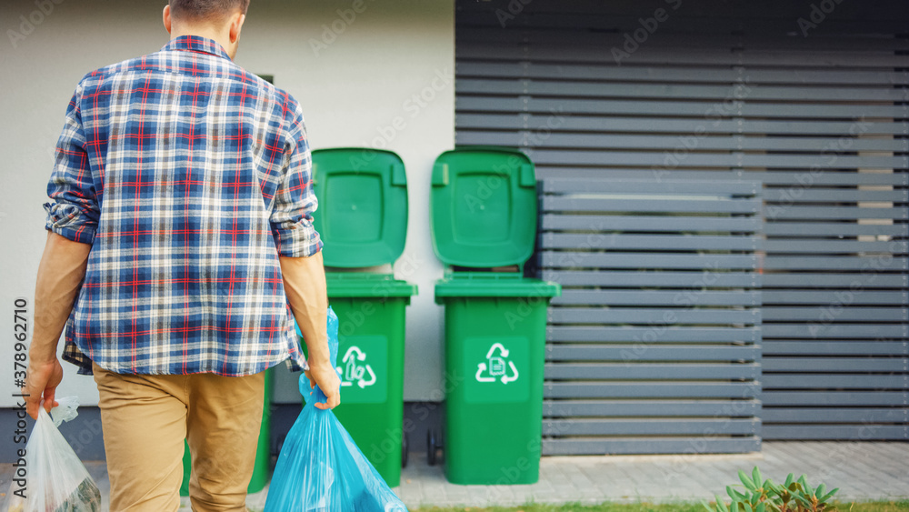 Caucasian Man is Walking Outside His House in Order to Take Out Two Plastic Bags of Trash. One Garba