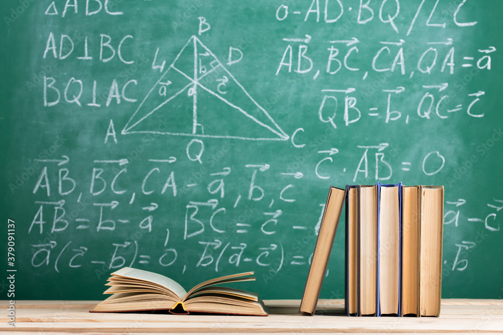 Education and reading concept - group of books on the wooden table, green blackboard with formulas o