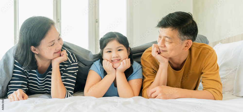 asian Senior grandparents couple laying with grandchildren preety female child on bed in bedroom,hap