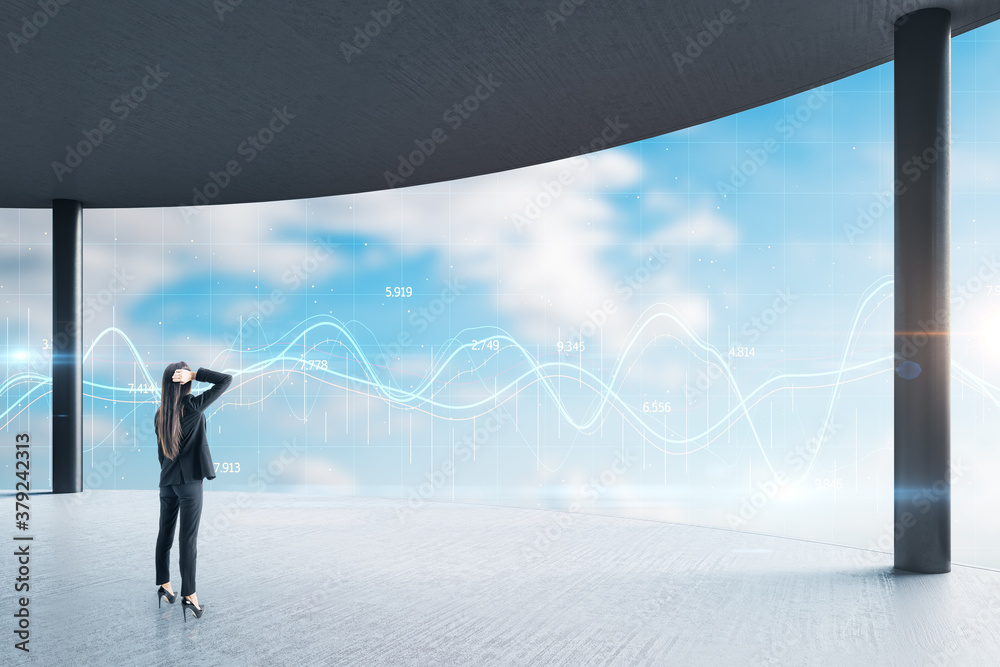 Businesswoman standing in office with glowing chart hologram in window.