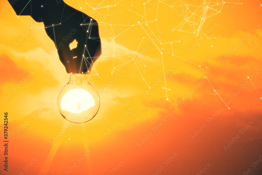 Hand holding glowing polygonal light bulb on sunset background.