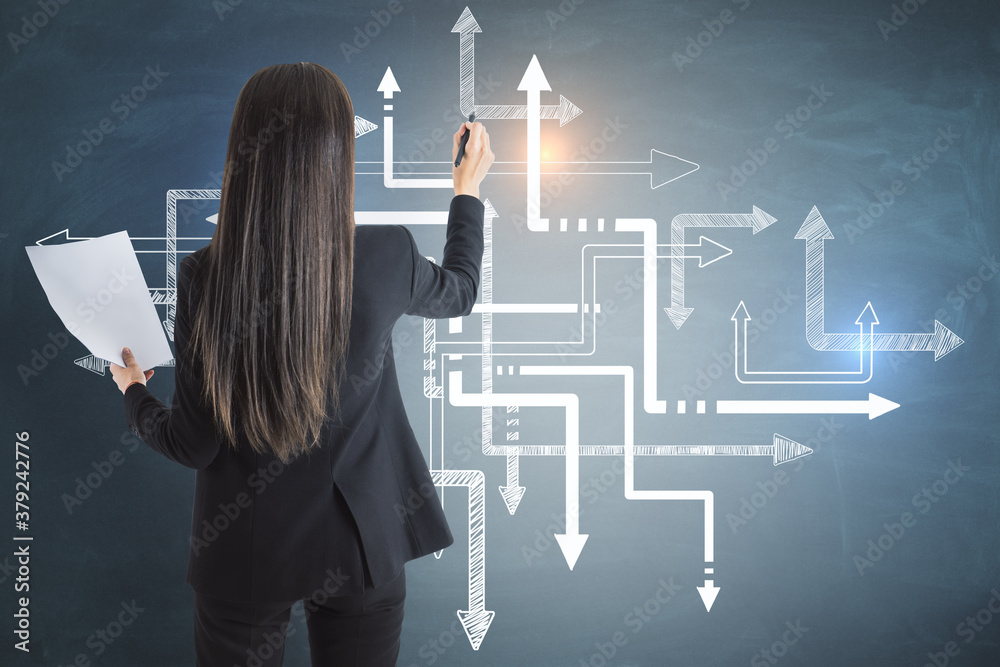 Businesswoman drawing arrows on gray concrete wall.