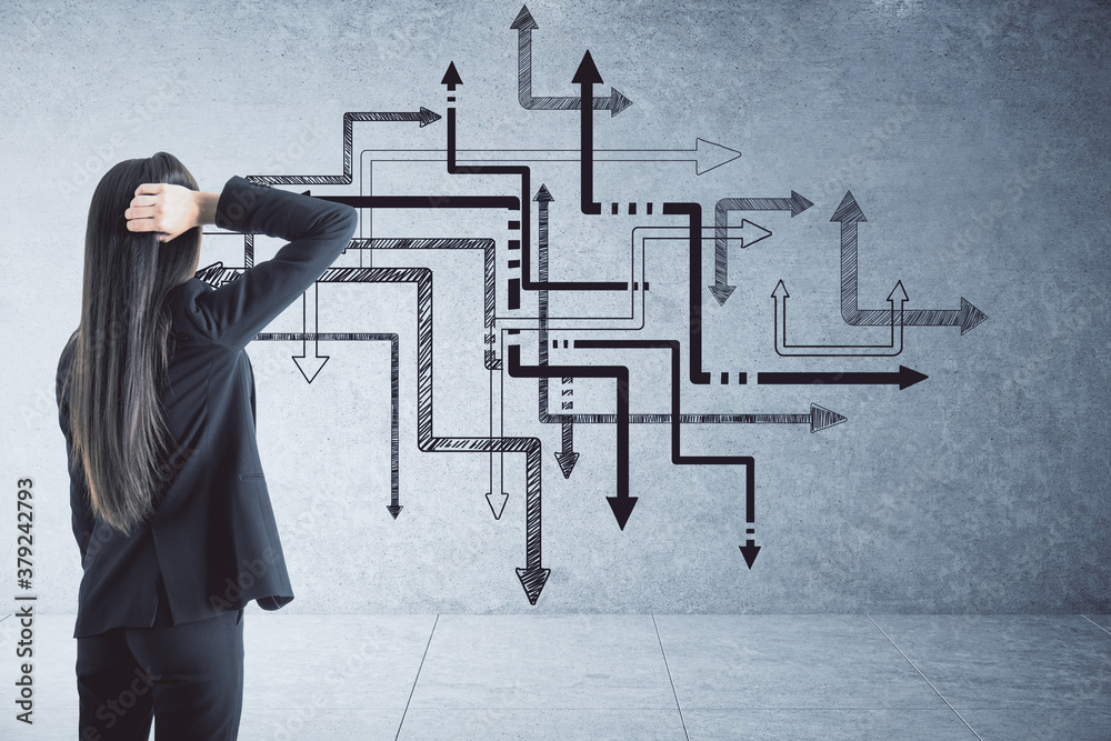 Businesswoman looking on drawing arrow system on concrete wall.