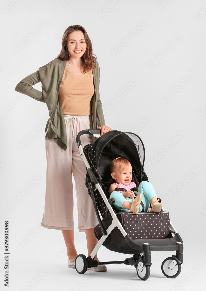 Woman and her cute baby in stroller on light background