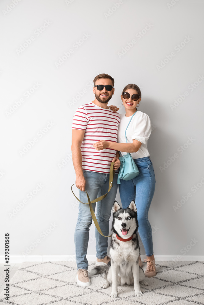 Young couple with cute Husky dog near light wall