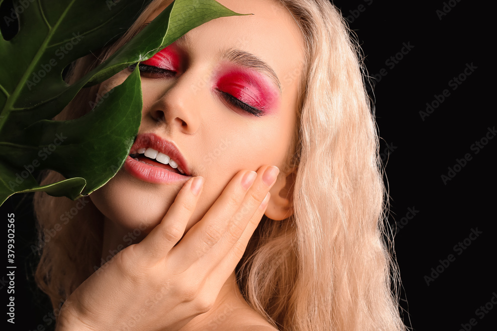 Young woman with beautiful eyeshadows and tropical leaf on dark background