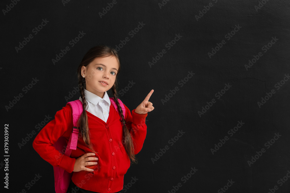 Little schoolgirl pointing at something on dark background