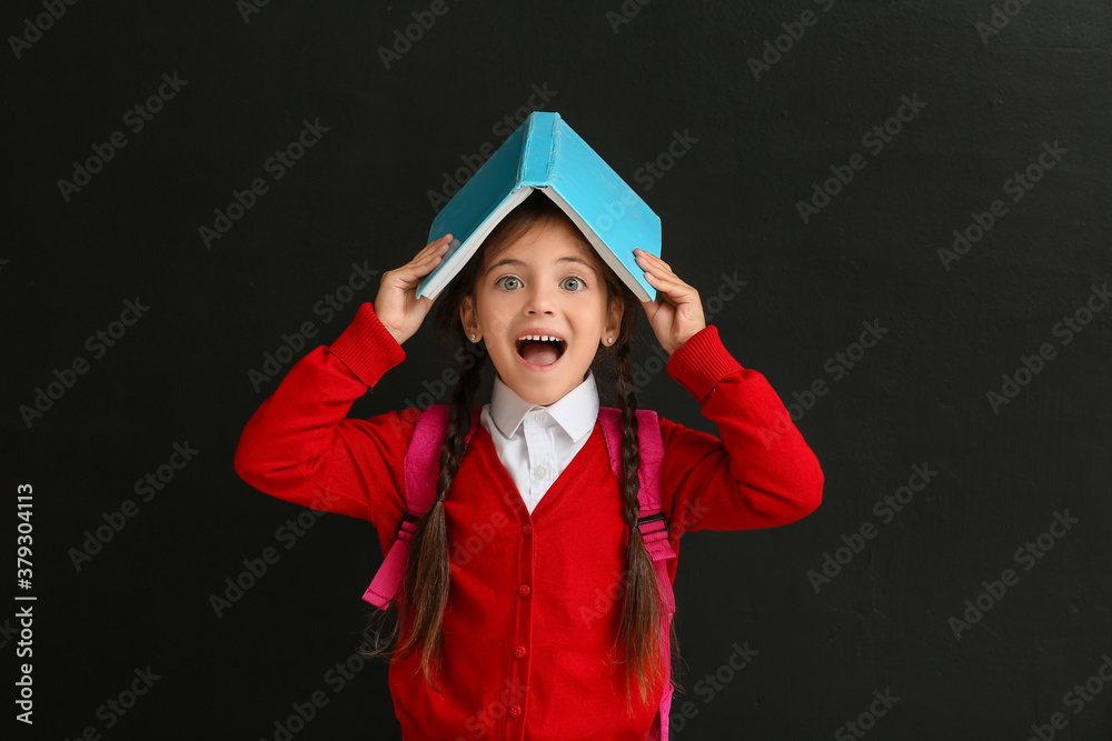 Little schoolgirl with book on dark background