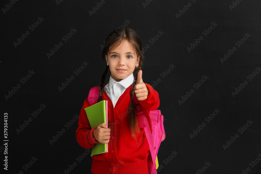 Little schoolgirl showing thumb-up on dark background