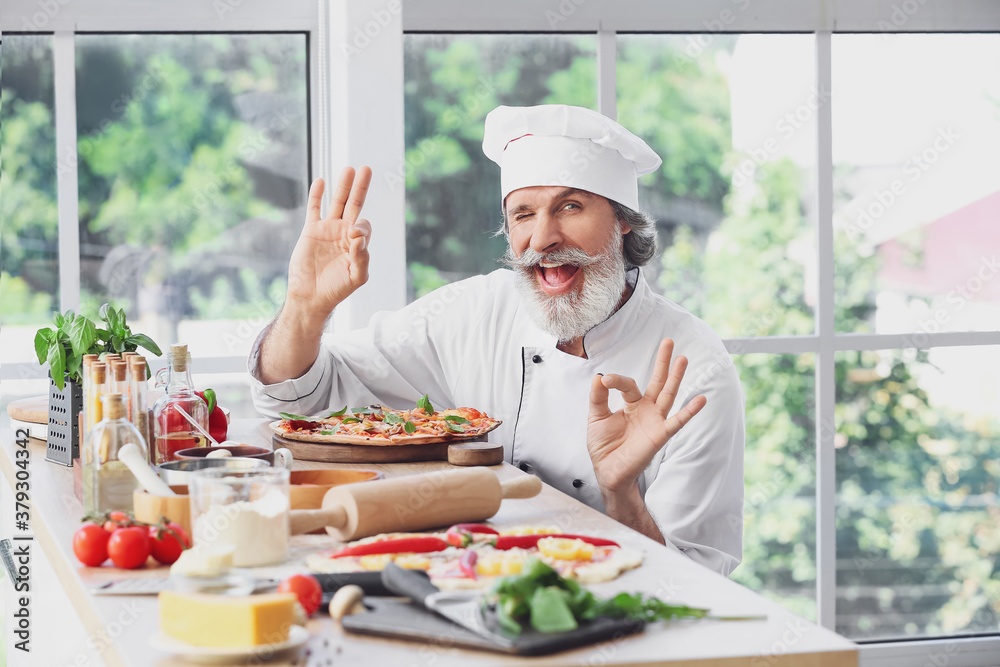 Mature male chef with tasty pizza in kitchen