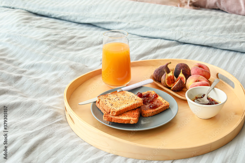 Tray with tasty breakfast on bed