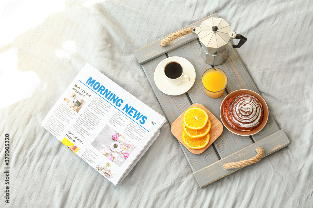 Tray with tasty breakfast and newspaper on bed