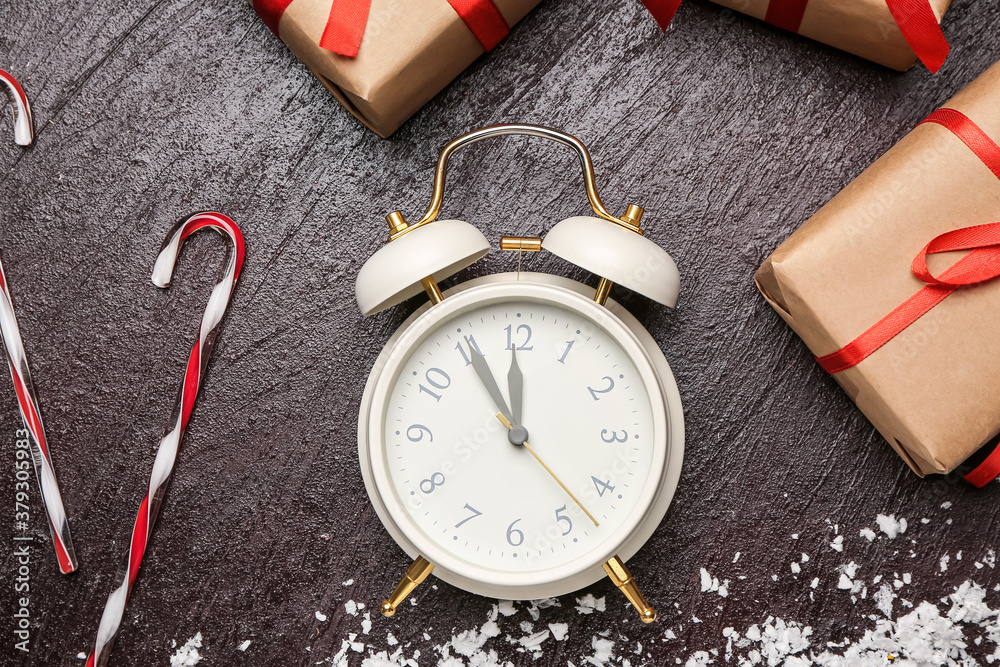 Alarm clock, candies and Christmas gifts on dark background