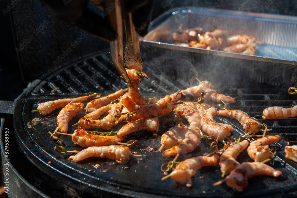 A professional cook prepares shrimps on the grill outdoor, food or catering concept