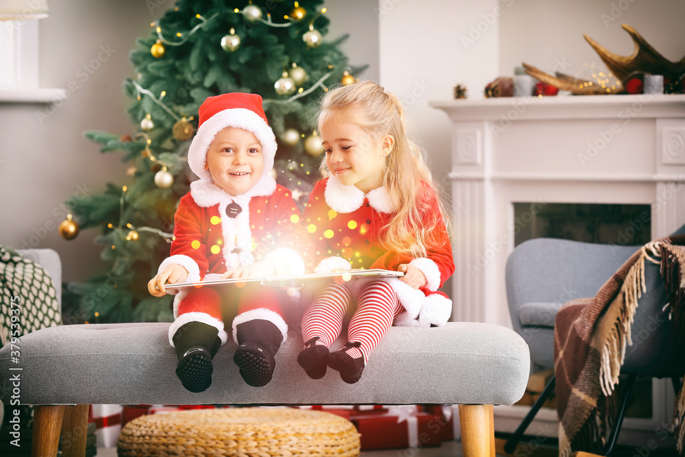 Cute little children in Santa costumes and with book at home on Christmas eve