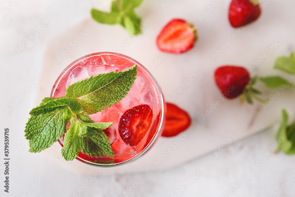 Glass of fresh strawberry mojito on light background