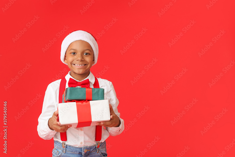 Cute African-American boy in Santa hat and with Christmas gifts on color background