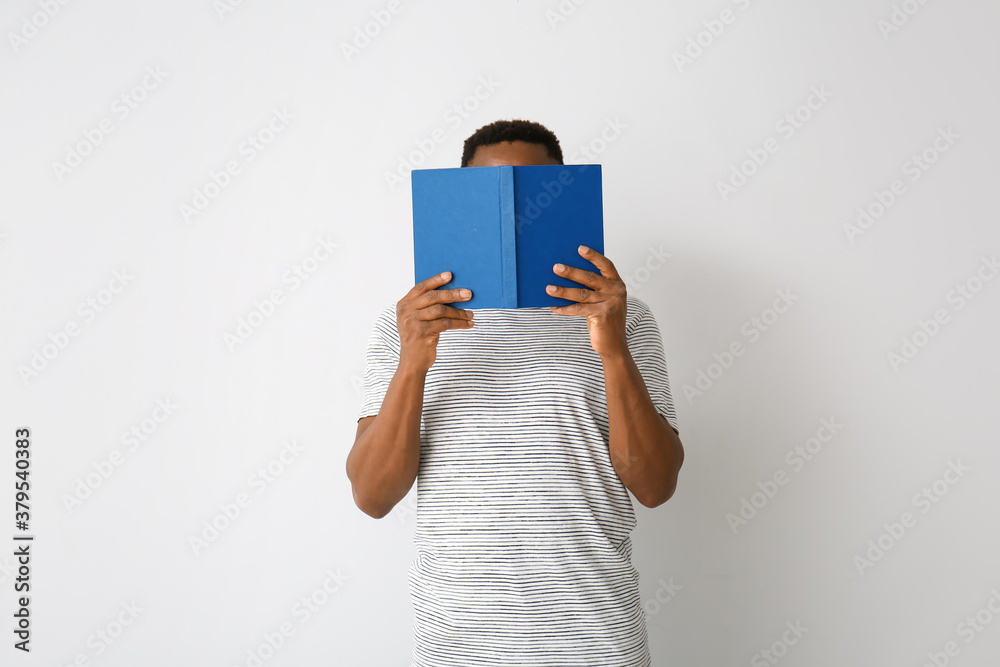 African-American man reading book on light background