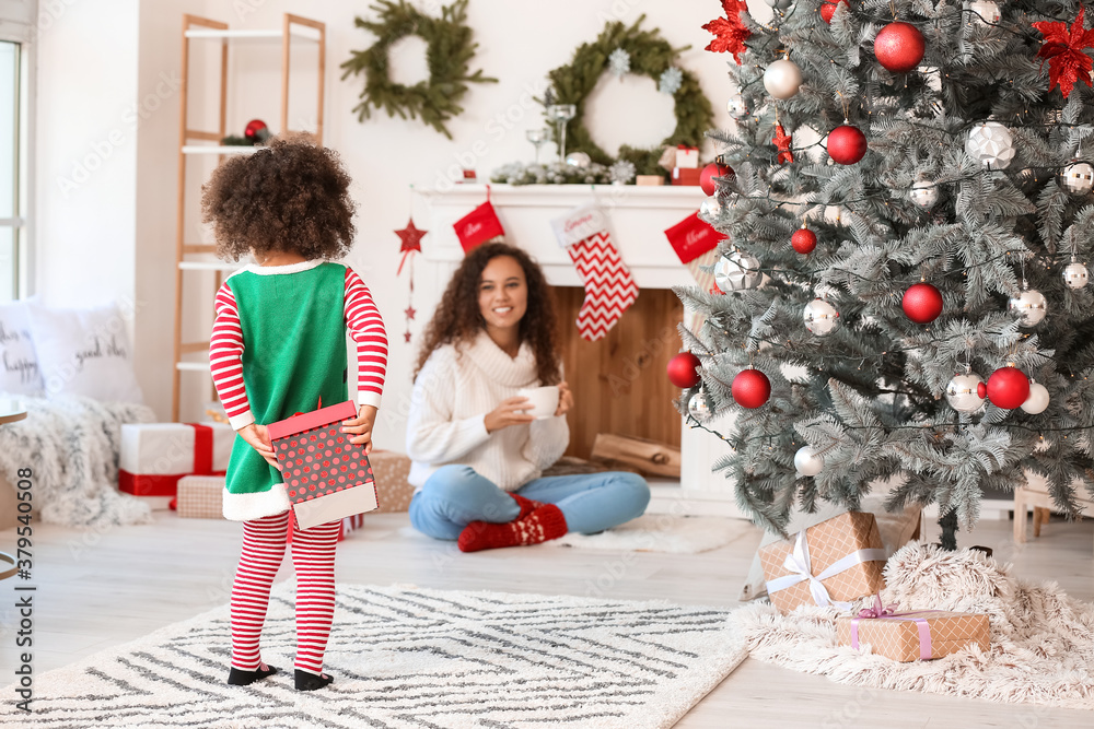 Cute African-American girl hiding gift for her mother on Christmas eve