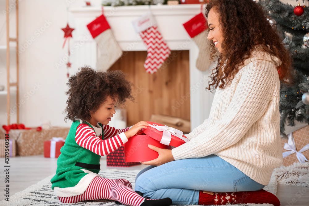 Cute African-American girl and her mother with Christmas gift at home