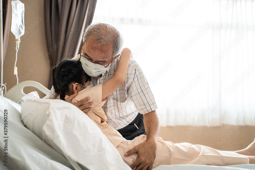 Asian old grandfather hugging little kid girl lying on bed in hospital