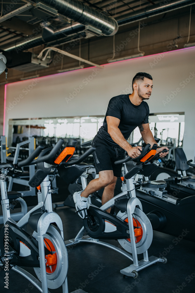 Sporty man riding spinning bikes at gym.