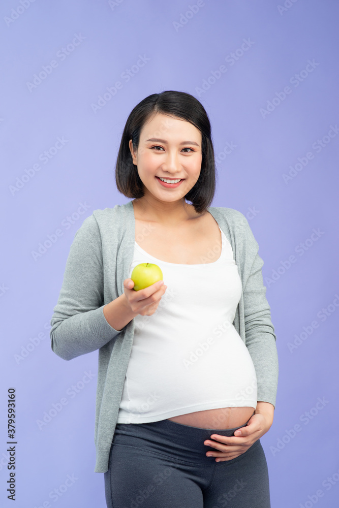 Image of a beautiful young pregnant woman posing isolated over purple wall background holding apple 