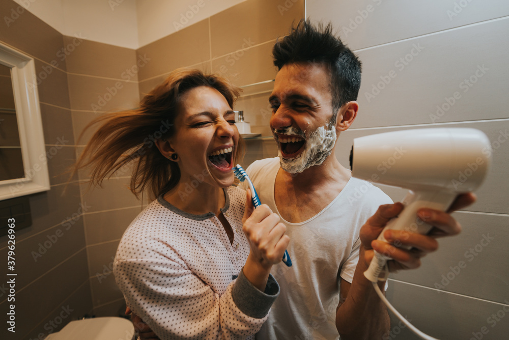 Happy young couple having fun together playing with shaving foam in the bathroom. Boyfriend and girl