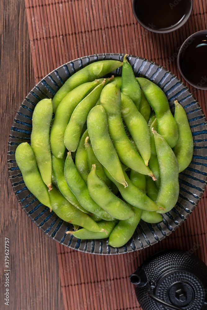 Fresh cooked boiled edamame in a plate on wooden tray and table background, healthy protein food con