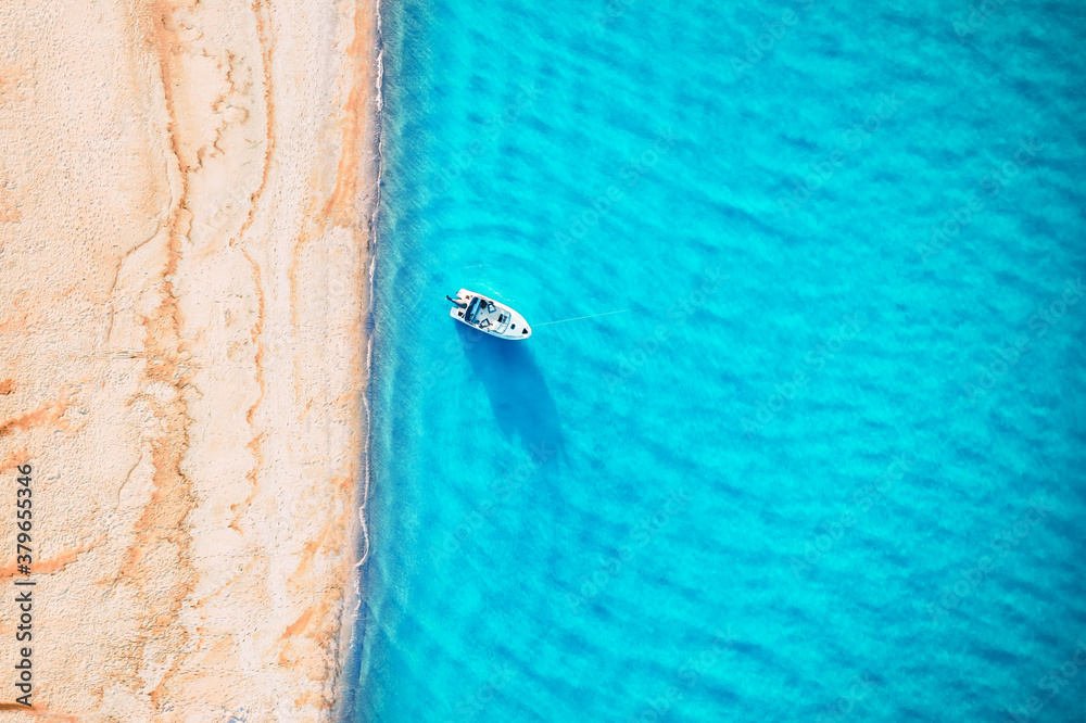 White yacht and turquoise water waves from top view. Beach with yellow sand glowing by sunlight. Tra