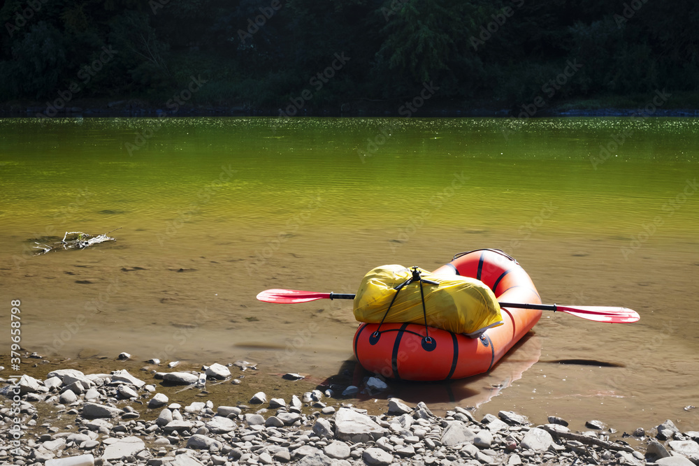 Orange packraft rubber boat with backpack on a river. Packrafting. Active lifestile concept