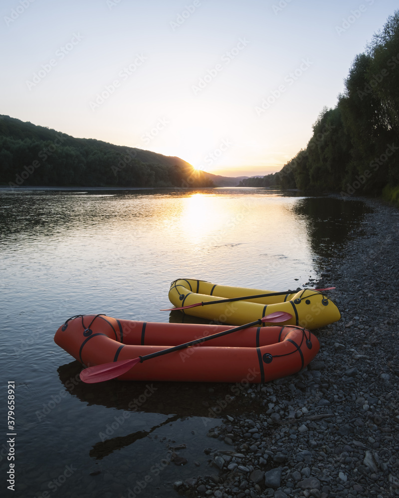 Orange and yellow packrafts rubber boats with padles on a sunrise river. Packrafting. Active lifesti