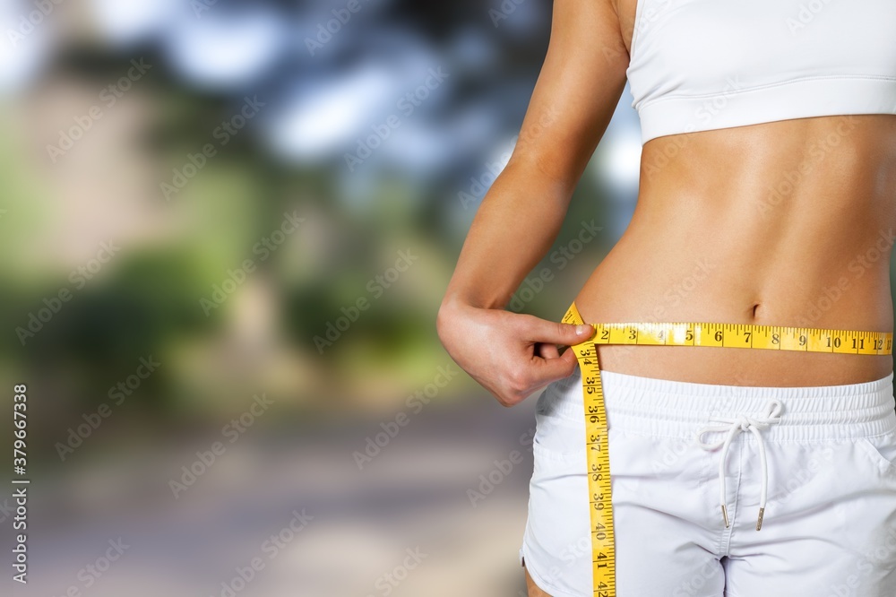 Slim young woman measuring her thin waist with a tape measure