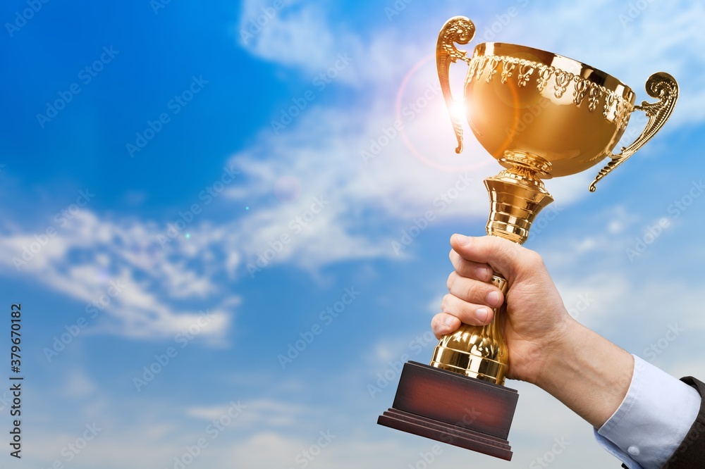 Hand holding golden trophy on the sky background